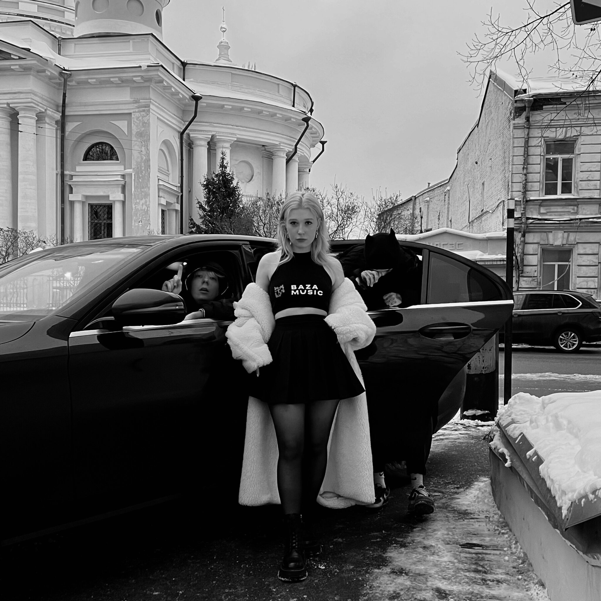 Зимнее чёрно-белое фото с EVEN CUTE в чёрной короткой юбке и чулках на фоне машины. Зимнее чёрно-белое фото с EVEN CUTE в чёрной короткой юбке и чулках на фоне машины.